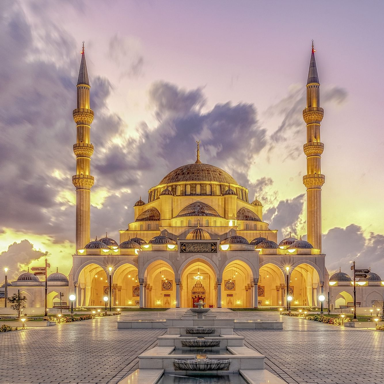 Illuminated Kocatepe Mosque with ornate architecture and surrounding landscape at dusk.