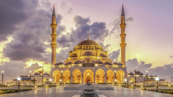 Illuminated Kocatepe Mosque with ornate architecture and surrounding landscape at dusk.