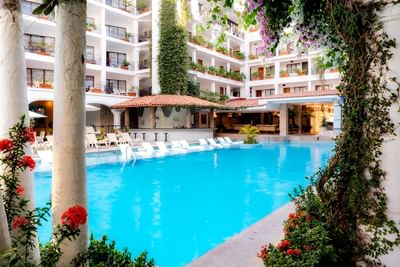 Bright blue pool surrounded by white hotel balconies with flowering vines and poolside lounge chairs at Playa Los Arcos