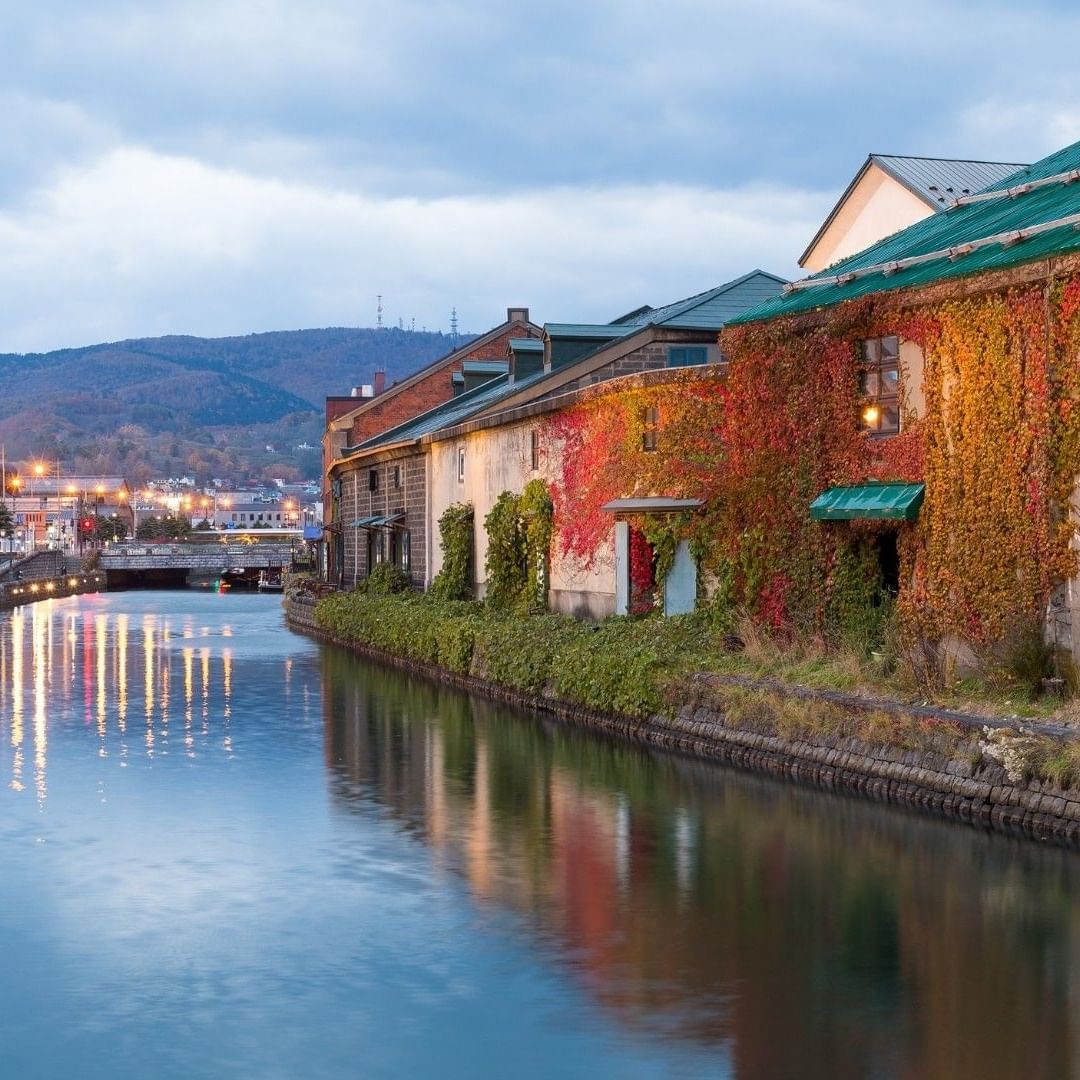 Streetlights reflecting on Otaru Canal along ivy-covered brick buildings under dusk sky near Grand Park Otaru
