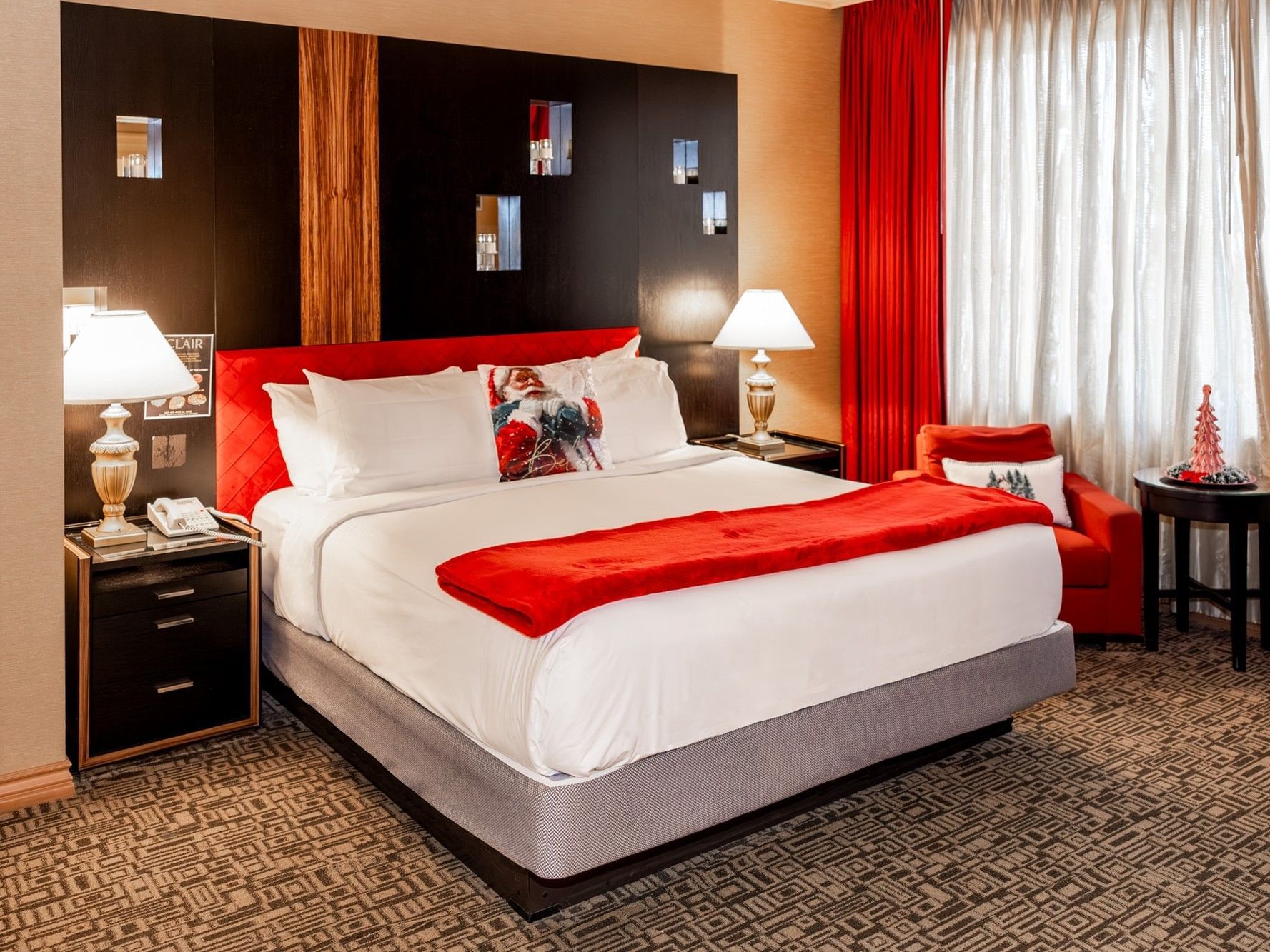 A luxurious hotel room with a large bed, red bedding, nightstands, lamps, red chair, and a window with curtains.