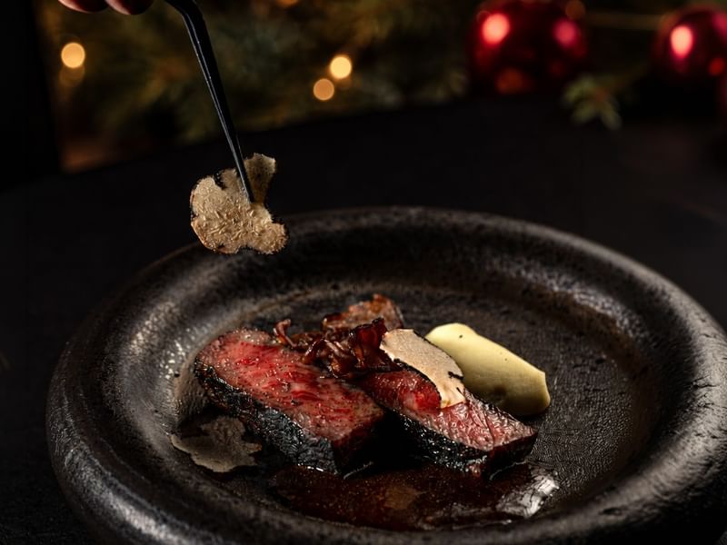 Jeff's Cellar gourmet A5 wagyu beef dish garnished with truffle shavings with festive red ornaments in the background celebrating New Years Eve