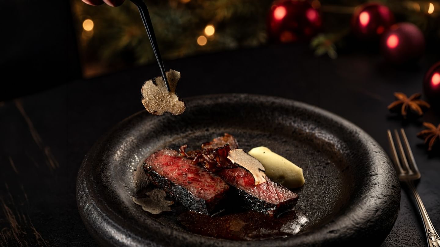Jeff's Cellar gourmet A5 wagyu beef dish garnished with truffle shavings with festive red ornaments in the background celebrating New Years Eve