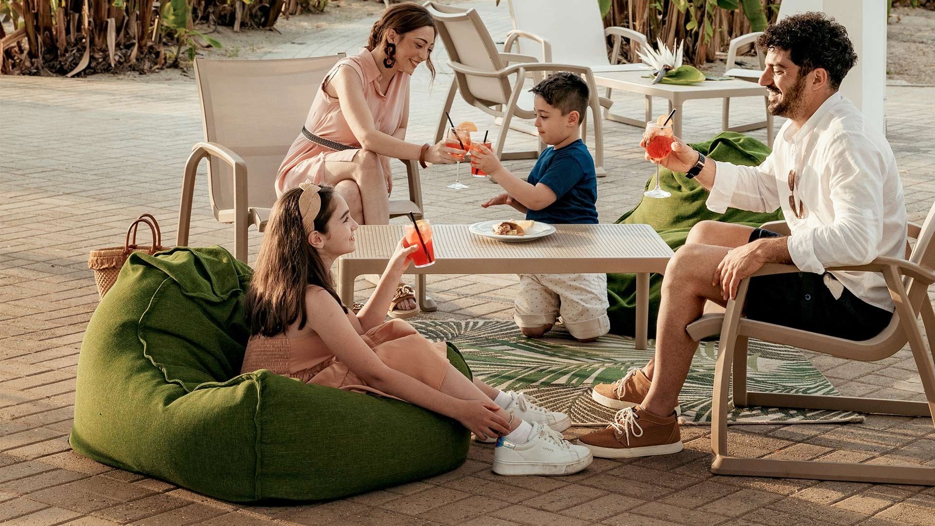 Familie genießt Getränke und Snacks auf grünen Sitzsäcken und Stühlen im Außenbereich.