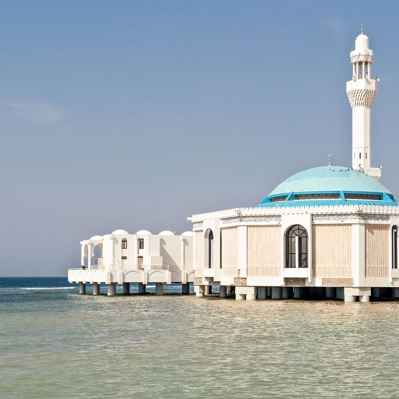 Jeddah Mosque with a turquoise dome and minaret stands over calm turquoise waters near Warwick Hotels and Resorts