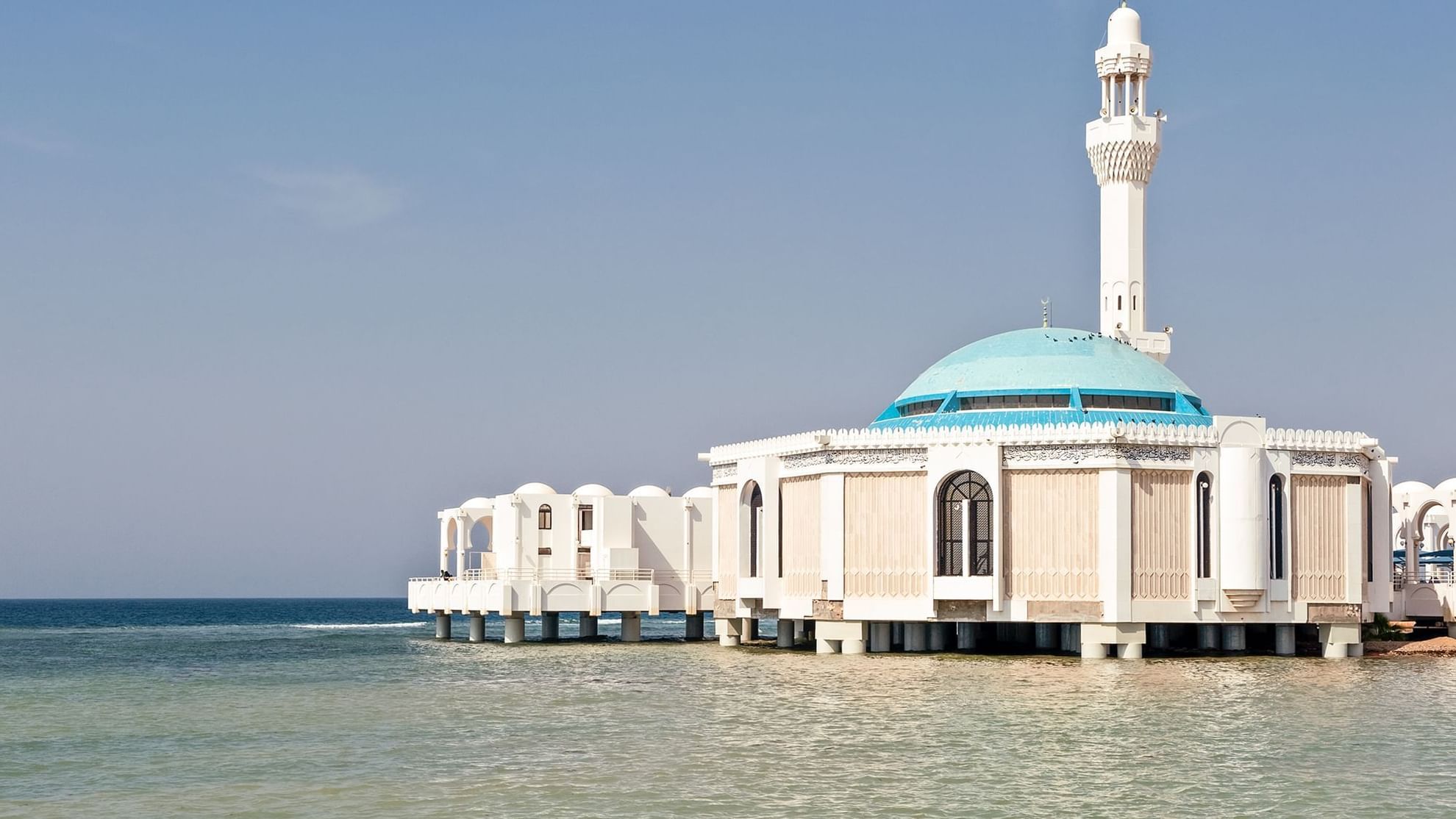 Jeddah Mosque with a turquoise dome and minaret stands over calm turquoise waters near Warwick Hotels and Resorts