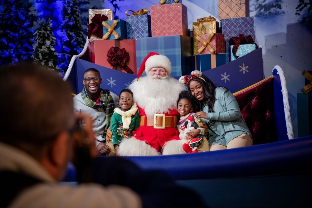 A family of four poses with Santa Claus in his sleigh as they have their photo taken. 