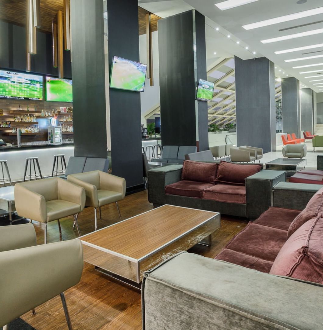 Armchairs by a wooden table under TVs near the illuminated bar counter in Stock Bar at Real Inn Tijuana