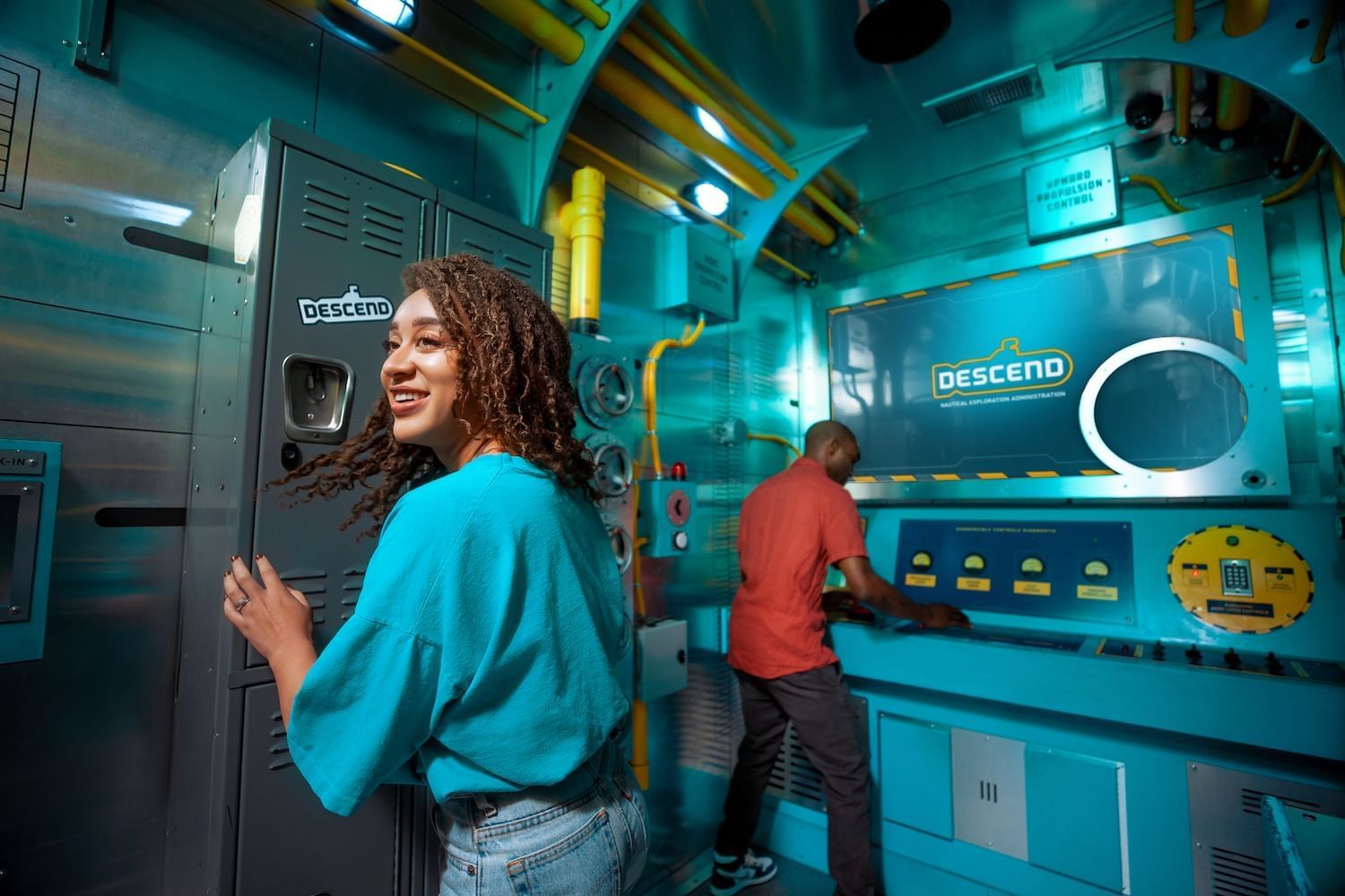 A man and a woman in a futuristic Escape Room with lockers and a computer system.