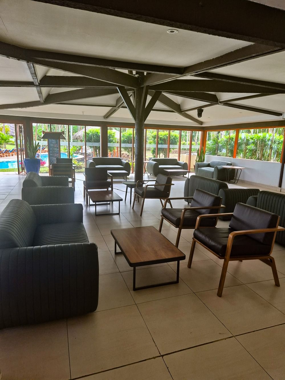 Newly refurbished lobby with modern seating, exposed beam ceiling, and views of the pool and tropical gardens beyond