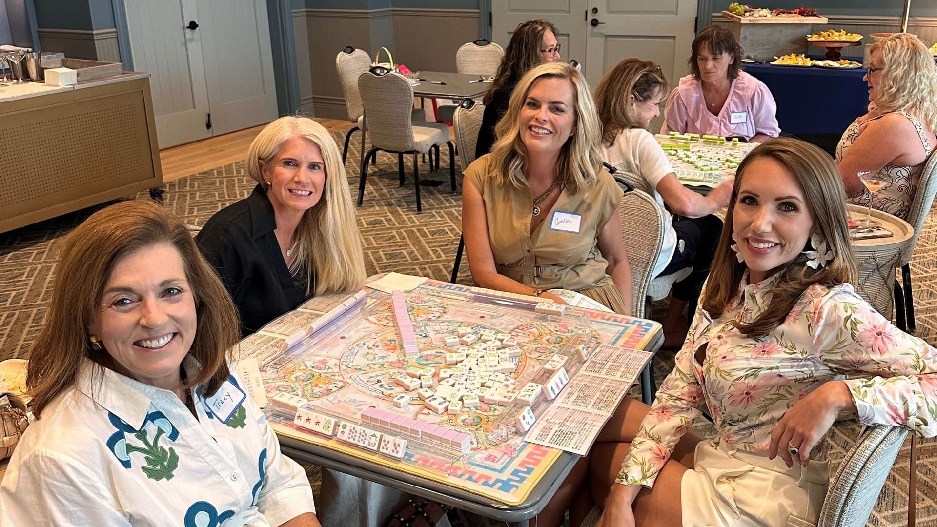 Women smiling and playing mahjong on a table at an event.