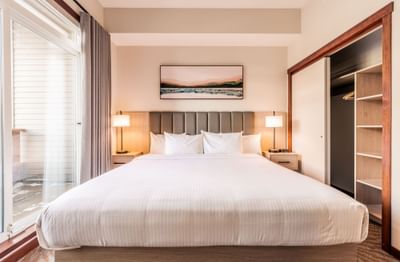 Nightstands and closet by comfy bed with cushioned headboard in One Bedroom Suite at Blackstone Mountain Lodge