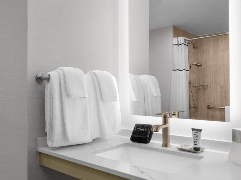 Capitol King room bathroom sink with plush towels, a brass faucet, and a large illuminated mirror at Hotel 43 Boise