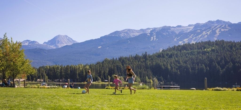 Family playing on the lawn by Alta Lake in Whistler with mountain views.