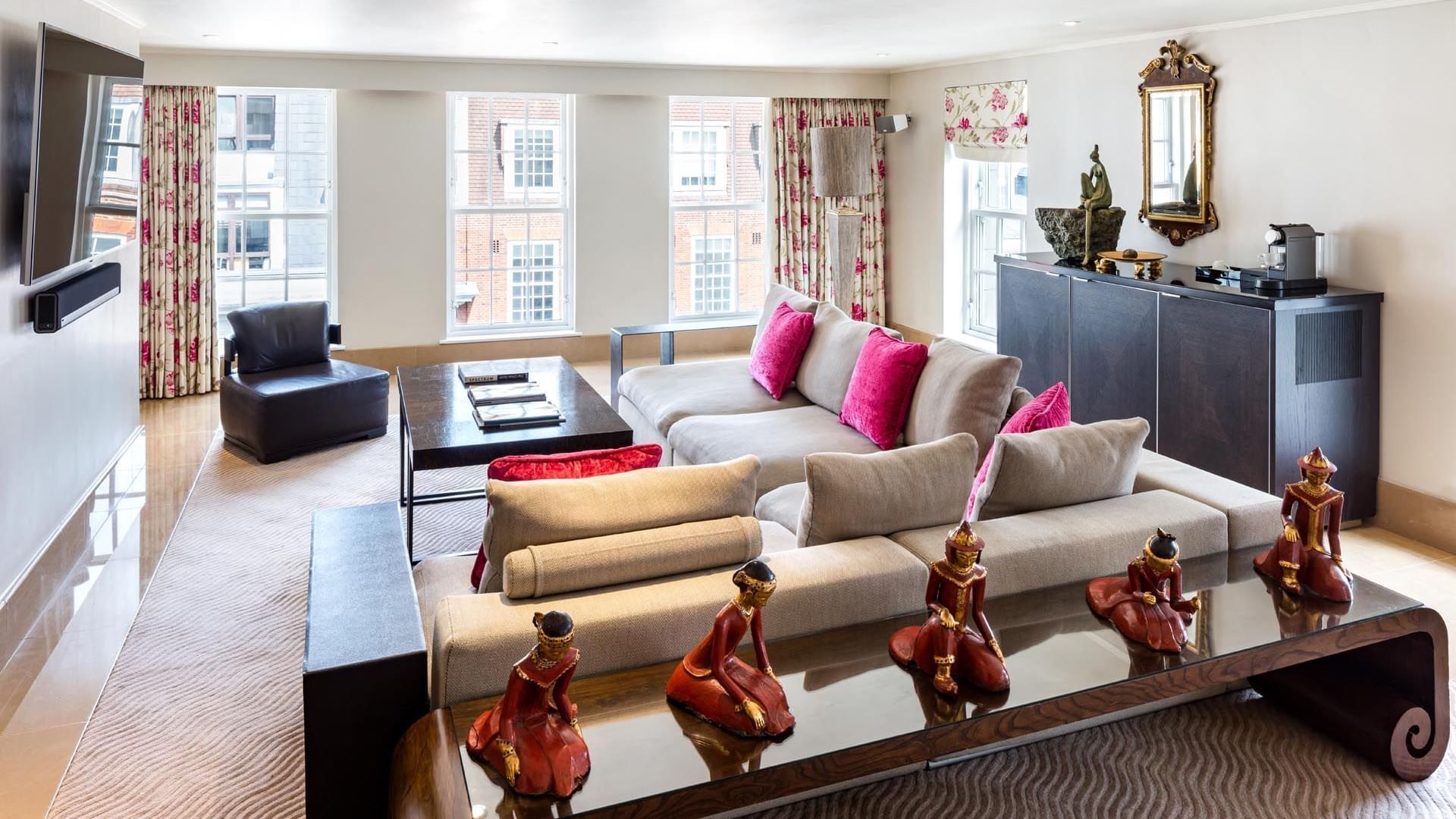 Elegant living room with beige sofas, pink cushions, an armchair, a decorative mirror, and large windows