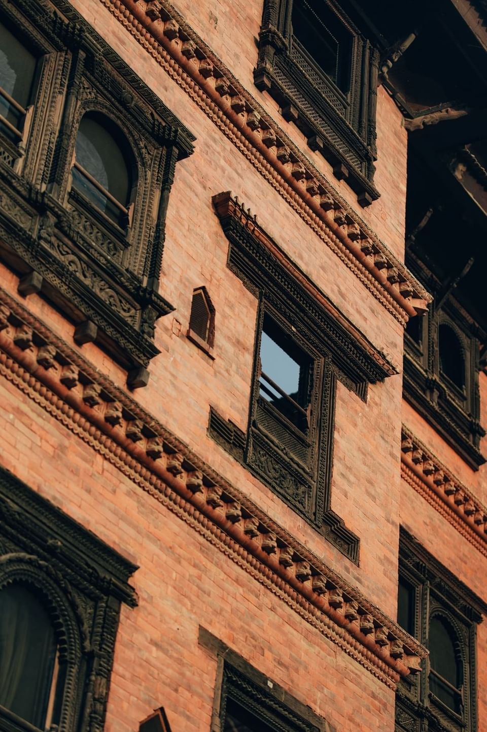 Brick building with ornate wooden window frames and intricate carvings on the facade at The Dwarika’s Hotels and Resorts