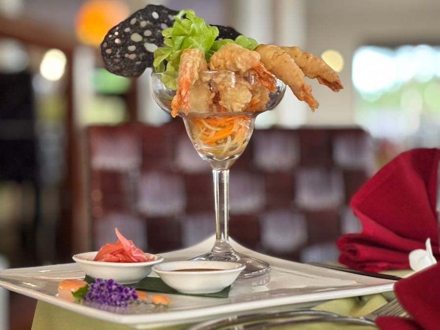 Shrimp dish with lettuce and sauce in a wine glass on a white plate at Warwick Le Lagon.