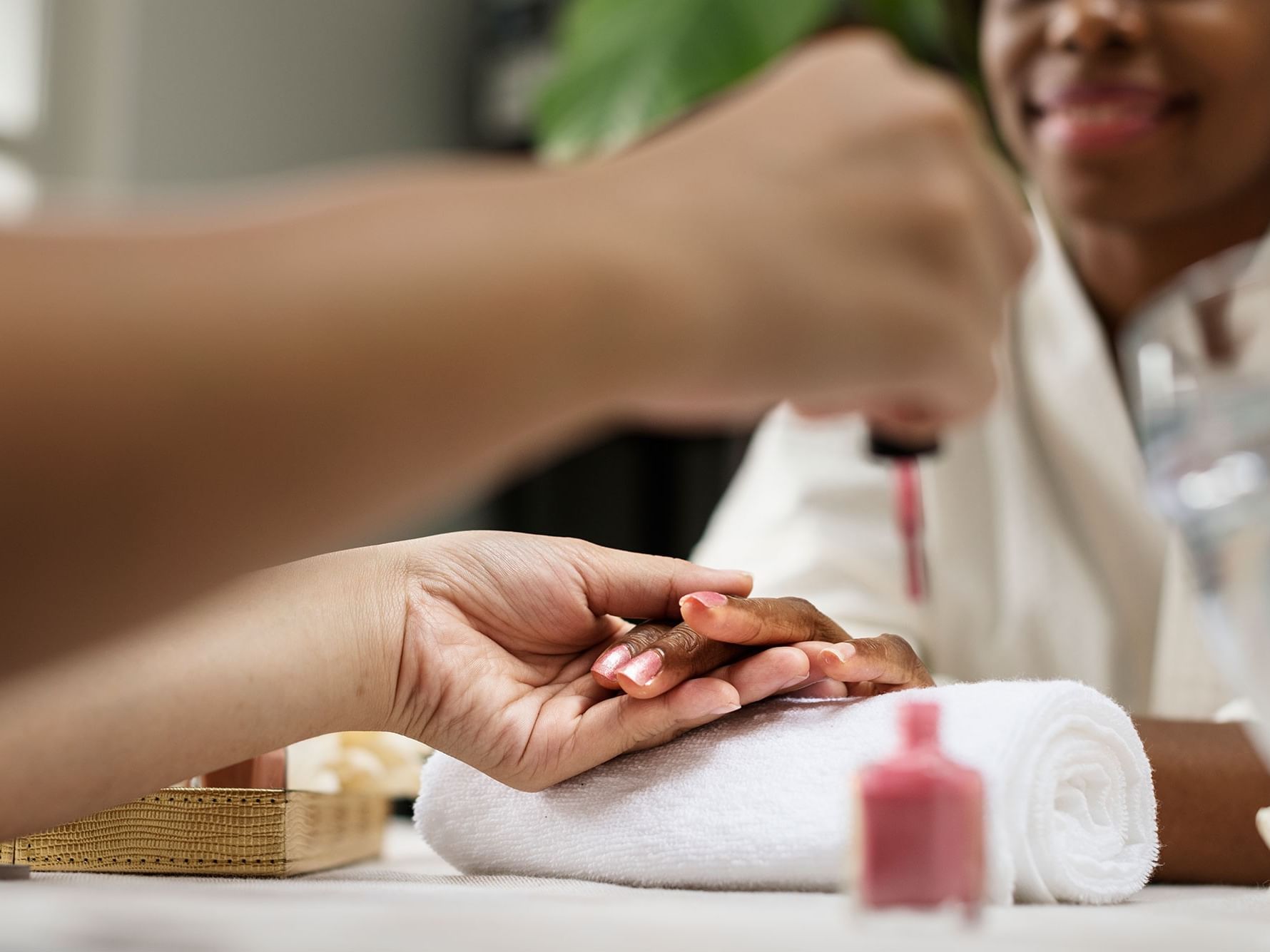 A woman getting her nails painted by a technician, with nail polish and towels visible.