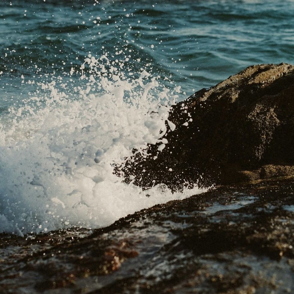 Ocean wave splashing and creating white foam against dark rocks near Falkensteiner Hotels & Residences