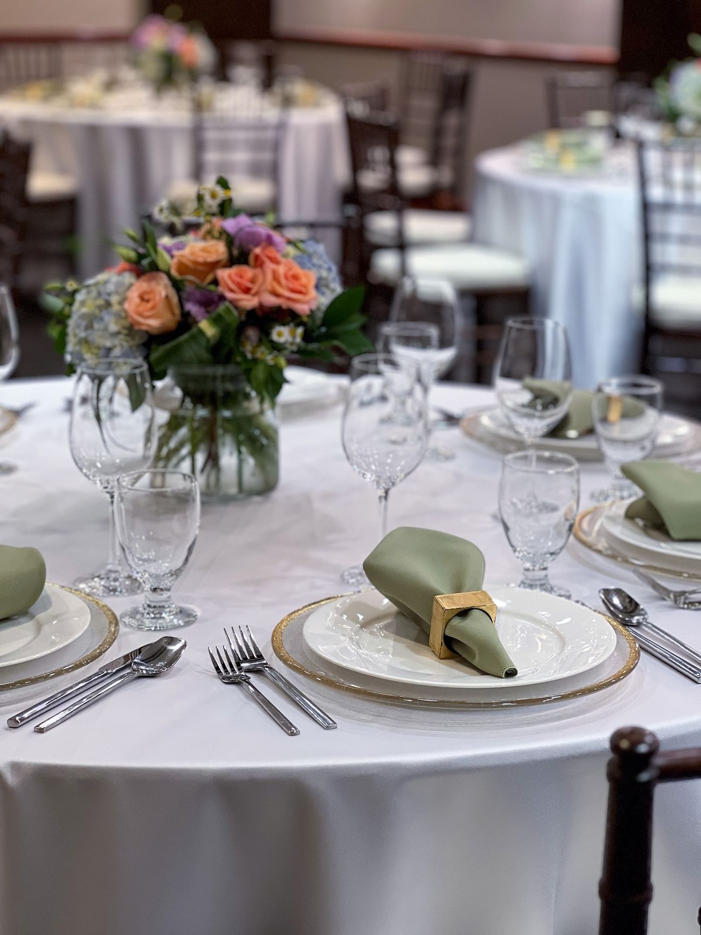 Sage napkins by silver cutlery and wine glasses surrounding floral centerpieces in Sasquatch Room B at Warwick Seattle