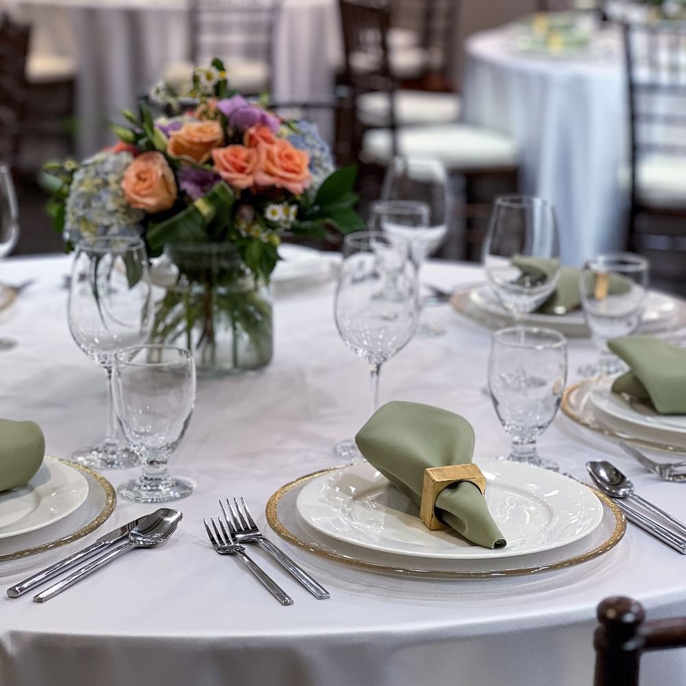Sage napkins by silver cutlery and wine glasses surrounding floral centerpieces in Sasquatch Room B at Warwick Seattle