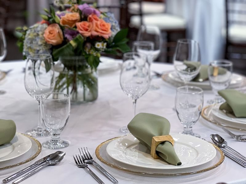 Sage napkins by silver cutlery and wine glasses surrounding floral centerpieces in Sasquatch Room B at Warwick Seattle
