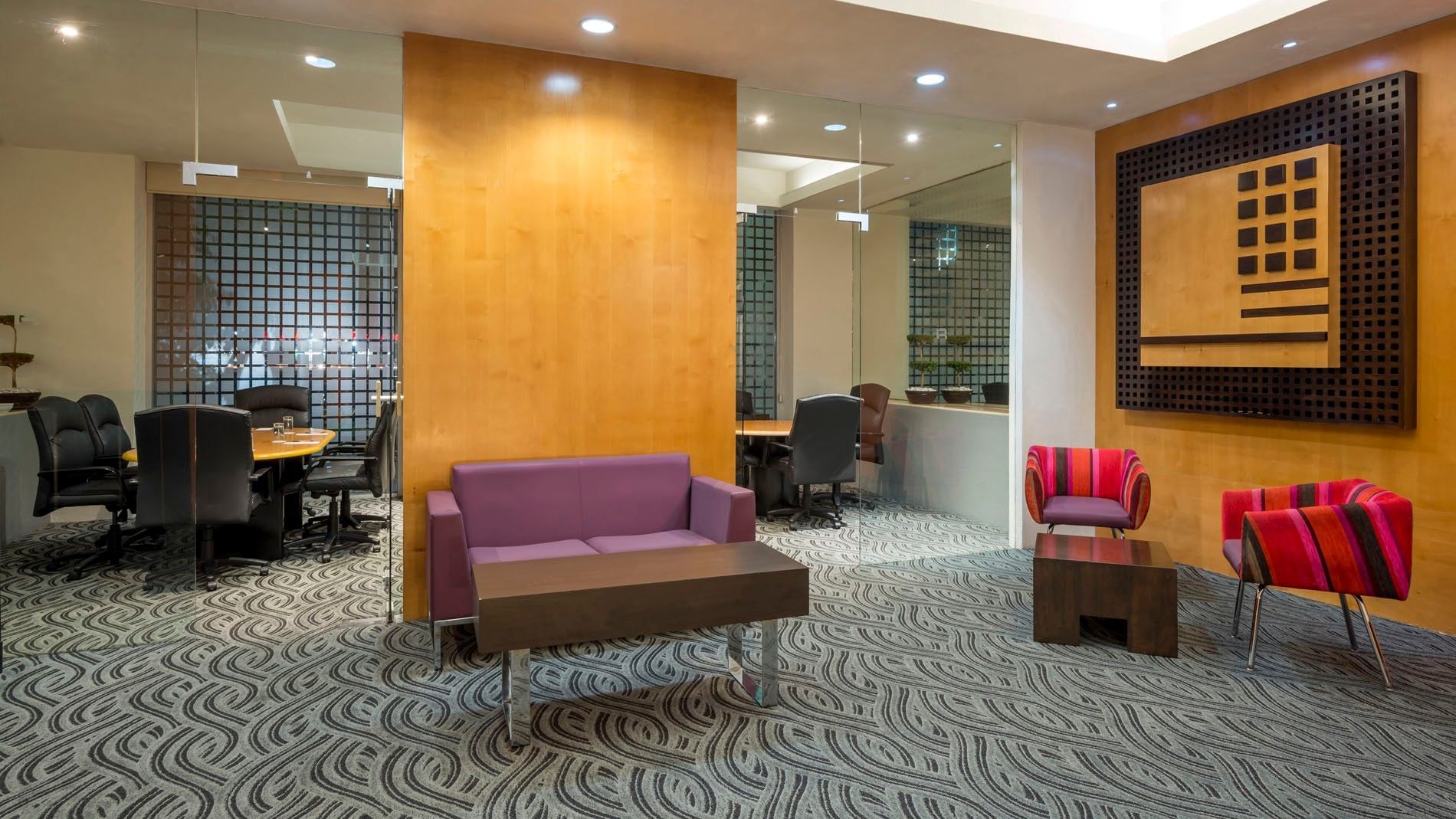 Modern lounge featuring purple sofas, colorful chairs, and glass-walled meeting rooms at Real Inn Perinorte