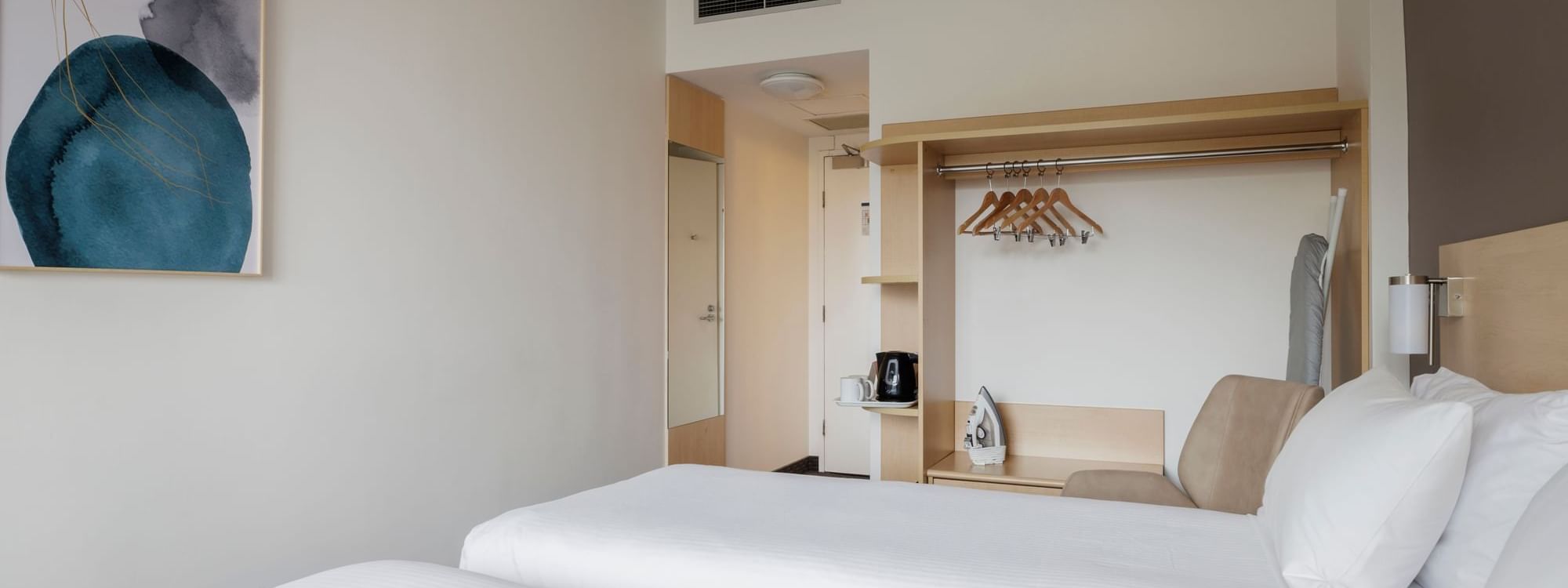 Comfy chair and closet with hangers by the beds in Standard Twin Room at Novotel Sydney Olympic Park