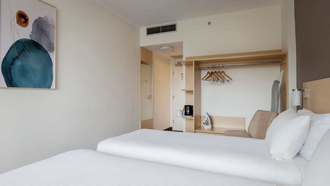 Comfy chair and closet with hangers by the beds in Standard Twin Room at Novotel Sydney Olympic Park