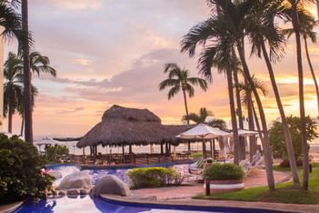 Sunset view of the poolside with lounge chairs at Plaza Pelicanos Grand Beach Resort