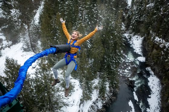 Woman bungee jumping off rope into snowy forest near Blackcomb Springs Suites