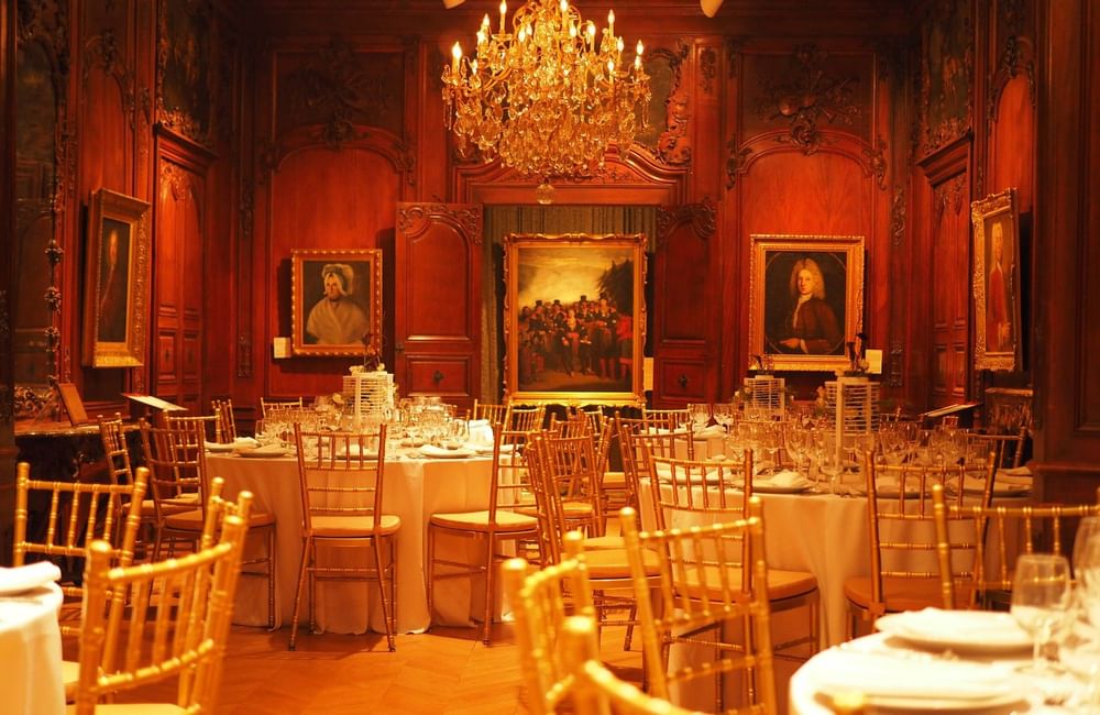 Elegant banquet hall with ornate wood paneling, crystal chandelier, classical paintings, and gold chiavari chairs at Warwick Le Crystal Montreal