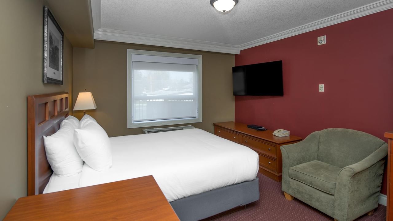 Guest room with white bedding, wooden furniture, green armchair, and wall-mounted TV at Coast Edson Hotel