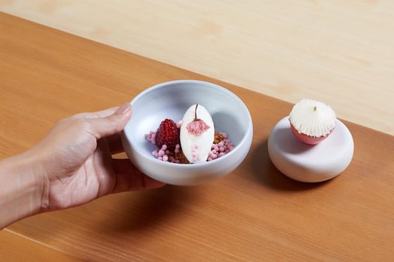 Hand holding a delicate bowl of dessert topped with a pink flower served at The Okura Prestige Bangkok