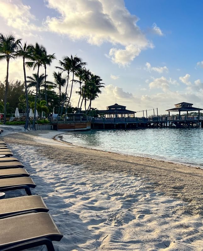Sandy beach by a wooden pier under a soft sky, surrounded by empty loungers at Warwick Paradise Island Bahamas