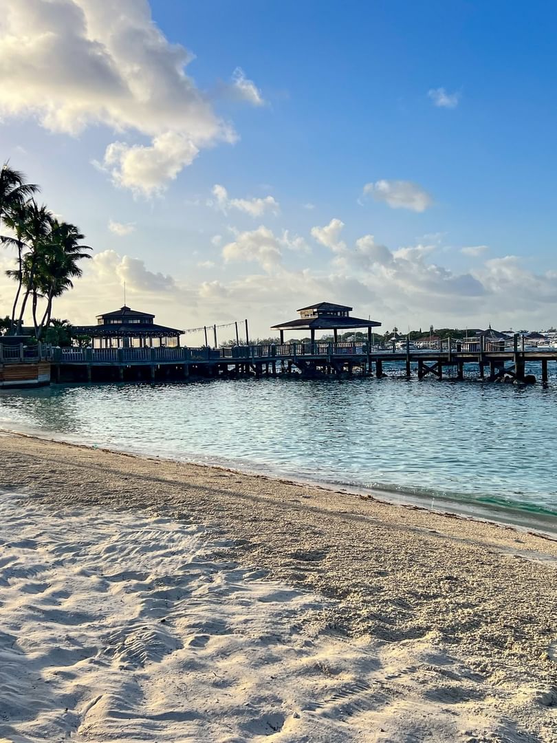 Sandy beach by a wooden pier under a soft sky, surrounded by empty loungers at Warwick Paradise Island Bahamas