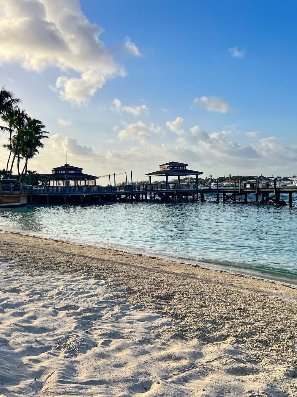 Sandy beach by a wooden pier under a soft sky, surrounded by empty loungers at Warwick Paradise Island Bahamas