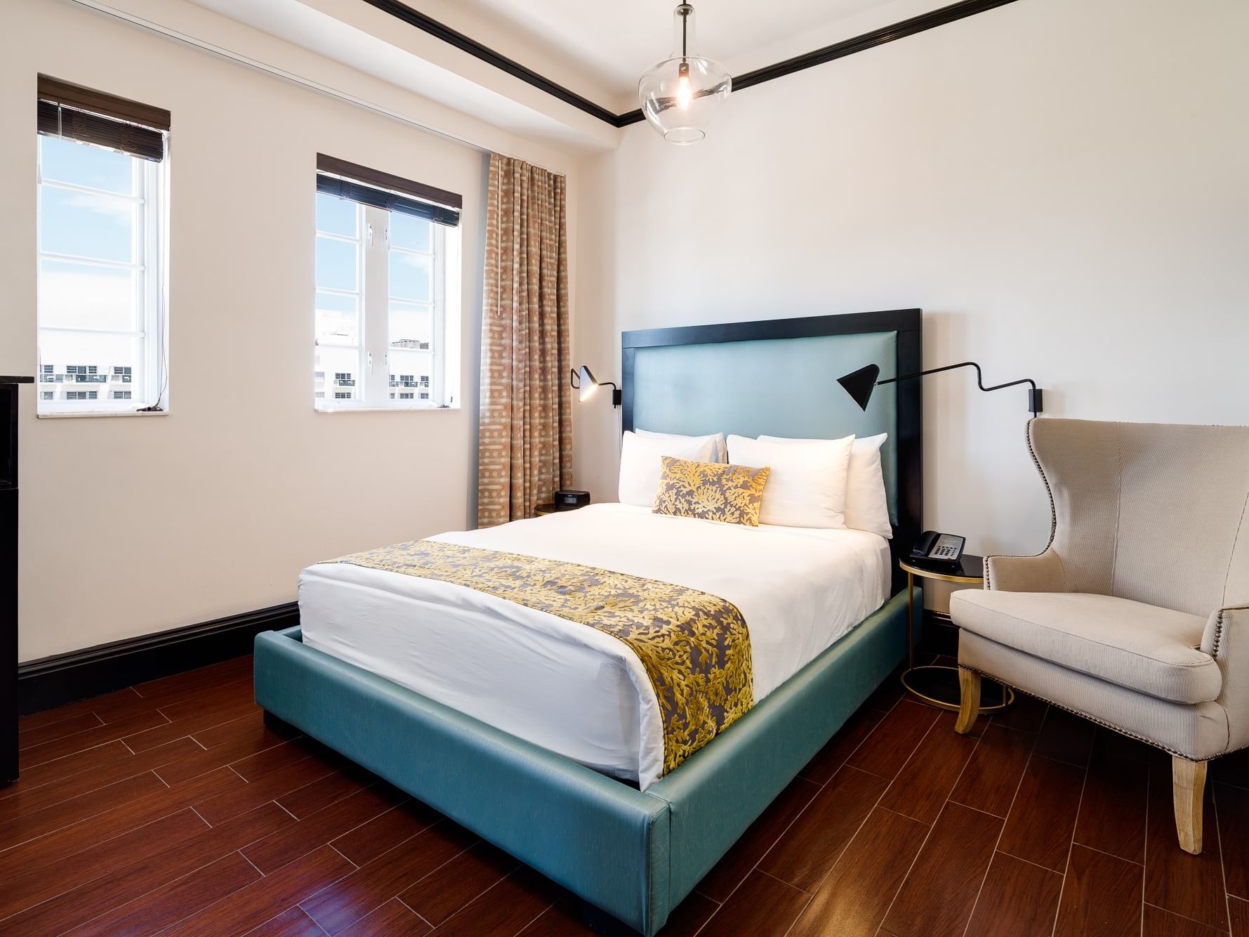 Classic Queen Room at Hotel Croydon Miami Beach with a queen bed, chair, wooden floor, and two windows with curtains