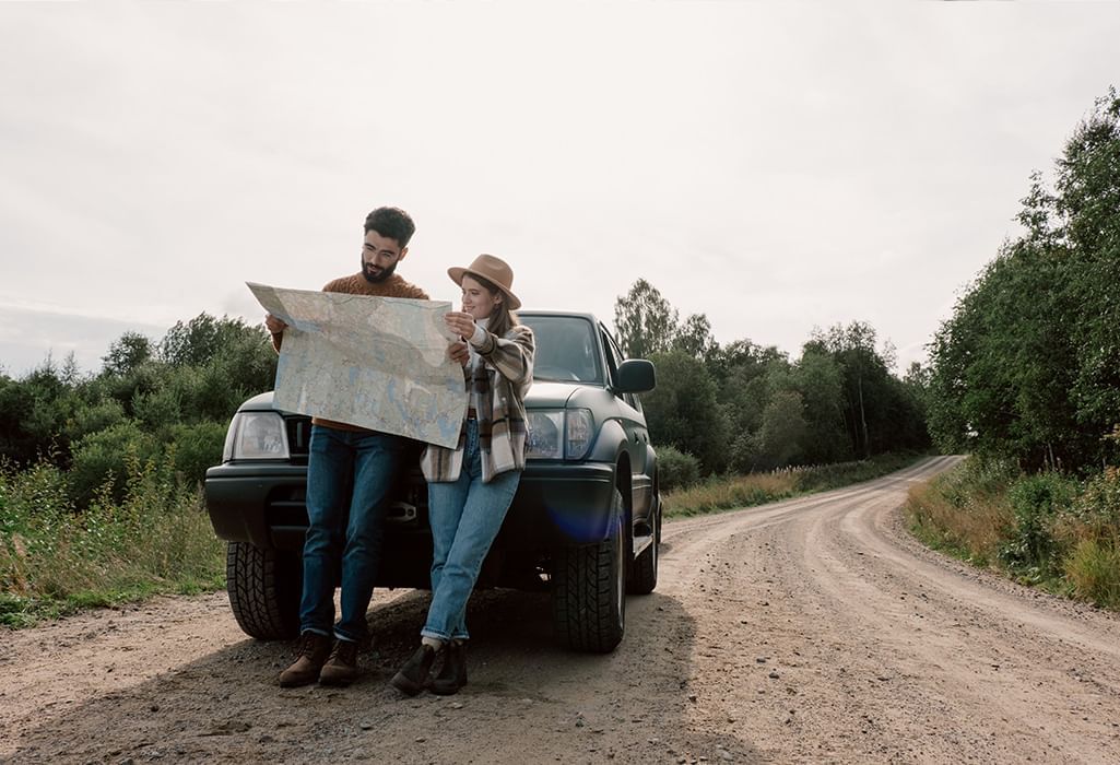 couple holding a map on a road trip by their car