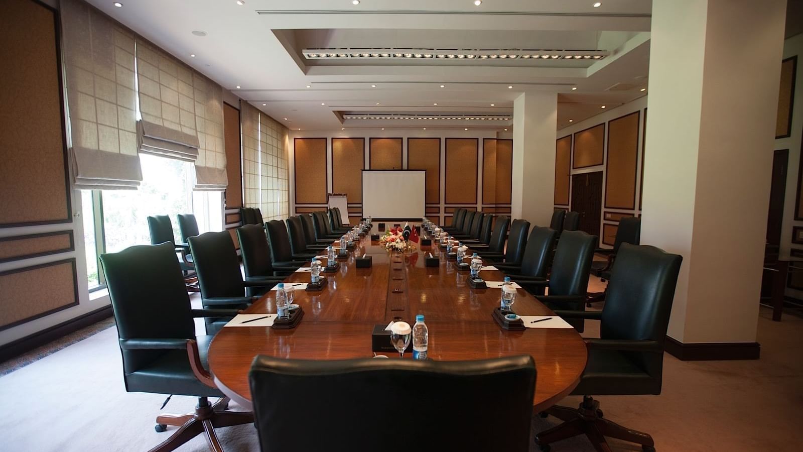 Polished oval boardroom table with black leather rolling chairs and projector screen at Serena Hotels & Resorts