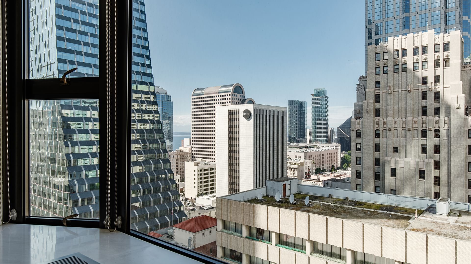 A city skyline view from a high-rise room with multiple skyscrapers visible under a clear blue sky.
