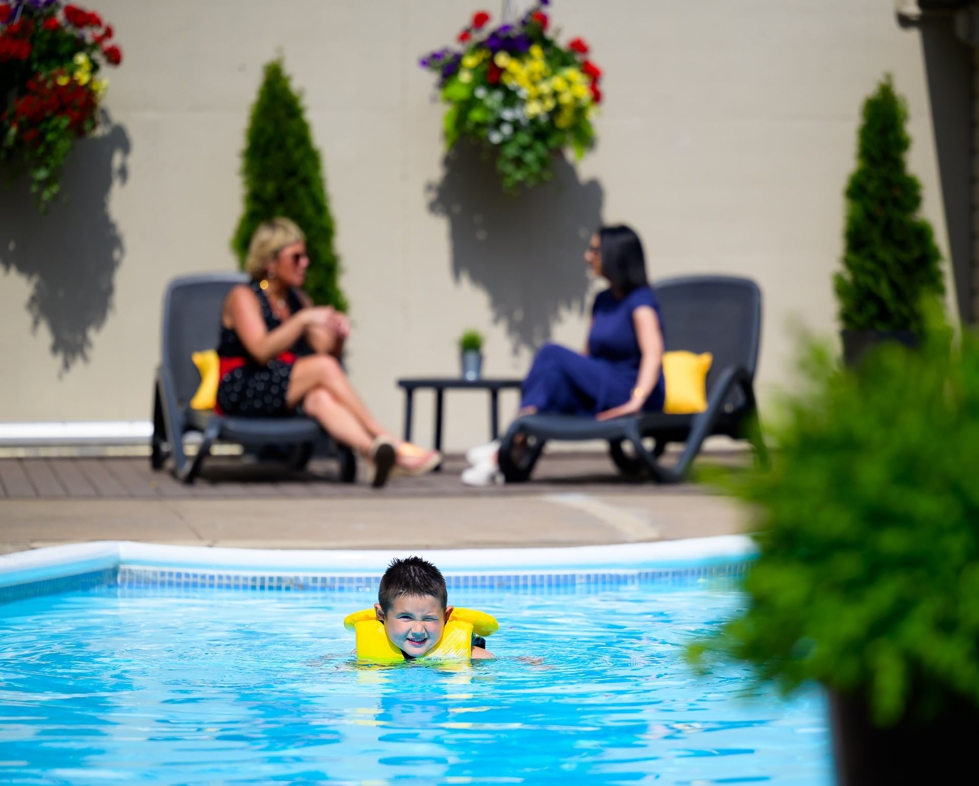 Child in yellow life jacket in pool with women on lounge chairs at Rodd Moncton, great things to do in Moncton