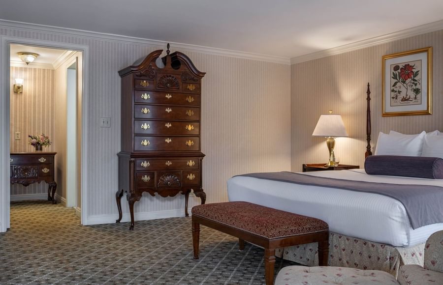 Ornate wooden dresser by a bed with a bolster pillow under a wall painting in Presidential Suite at Warwick Denver