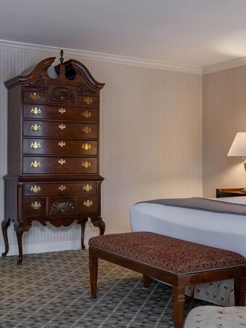Ornate wooden dresser by a bed with a bolster pillow under a wall painting in Presidential Suite at Warwick Denver
