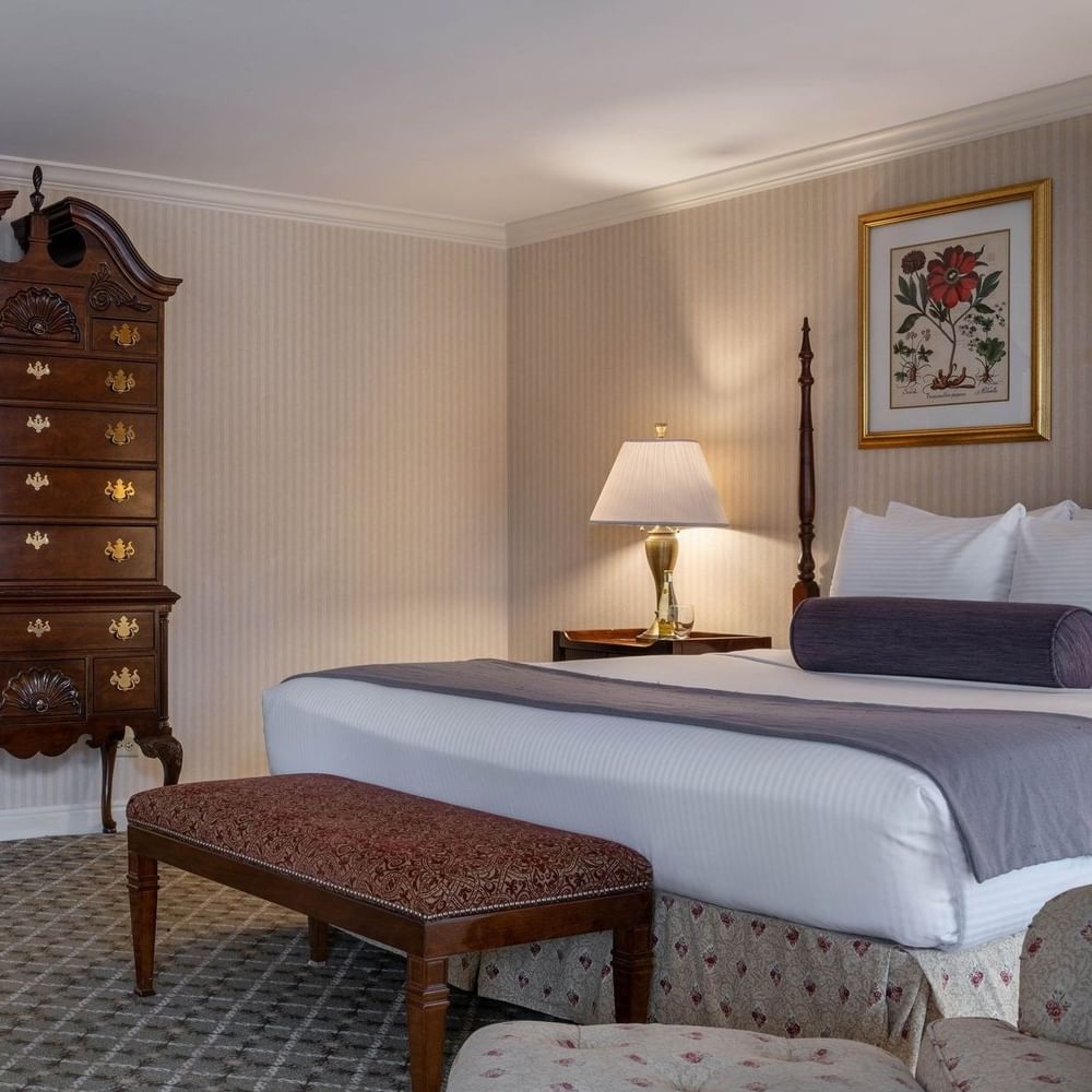 Ornate wooden dresser by a bed with a bolster pillow under a wall painting in Presidential Suite at Warwick Denver
