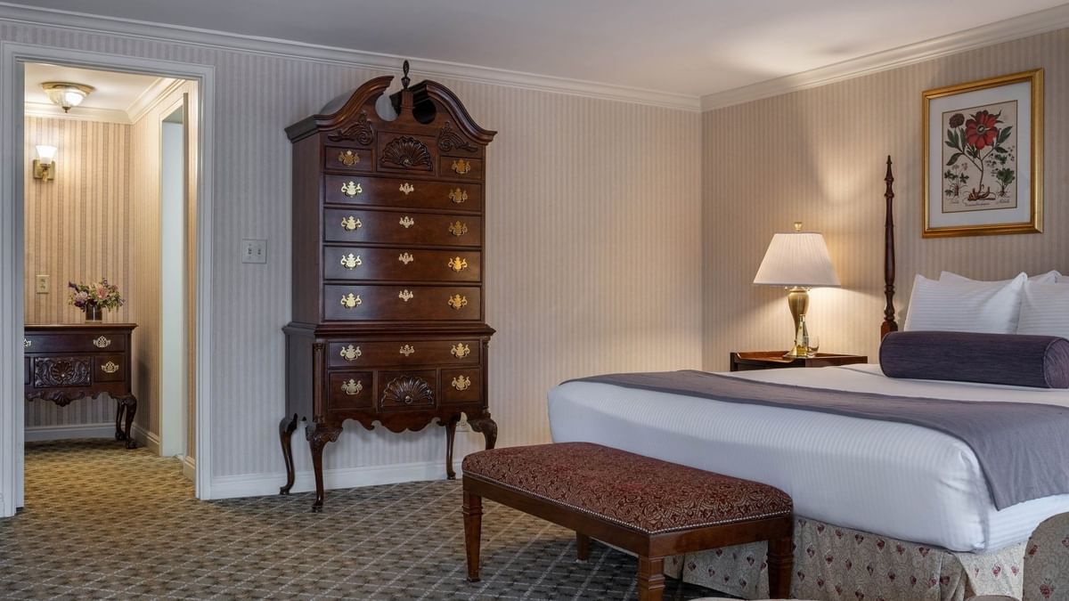 Ornate wooden dresser by a bed with a bolster pillow under a wall painting in Presidential Suite at Warwick Denver