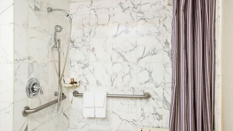 A bathroom with a showerhead, grab bars, and a striped curtain at Warwick Hotels and Resorts