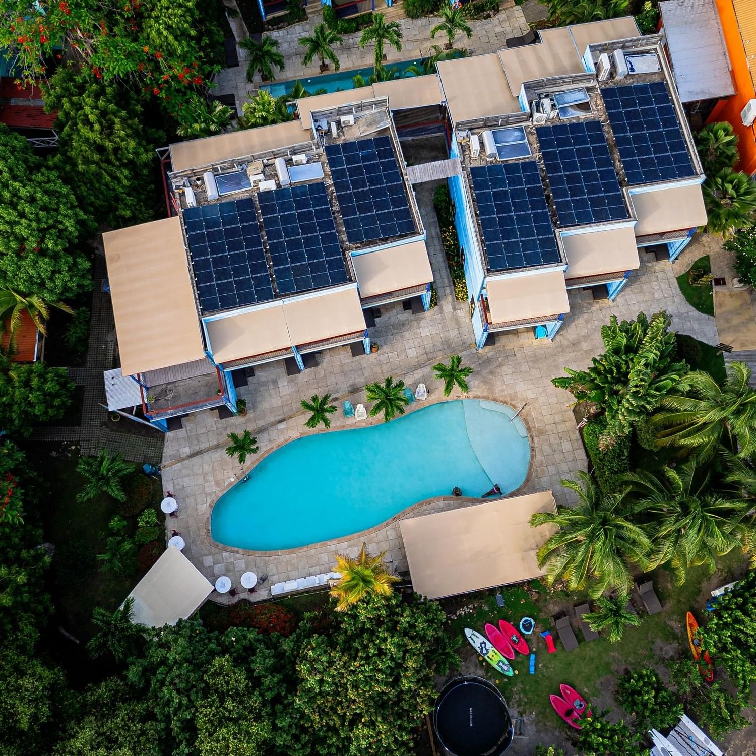 Aerial view of True Blue Bay Boutique Resort a sustainable resort with solar panels, pool, and lush greenery.