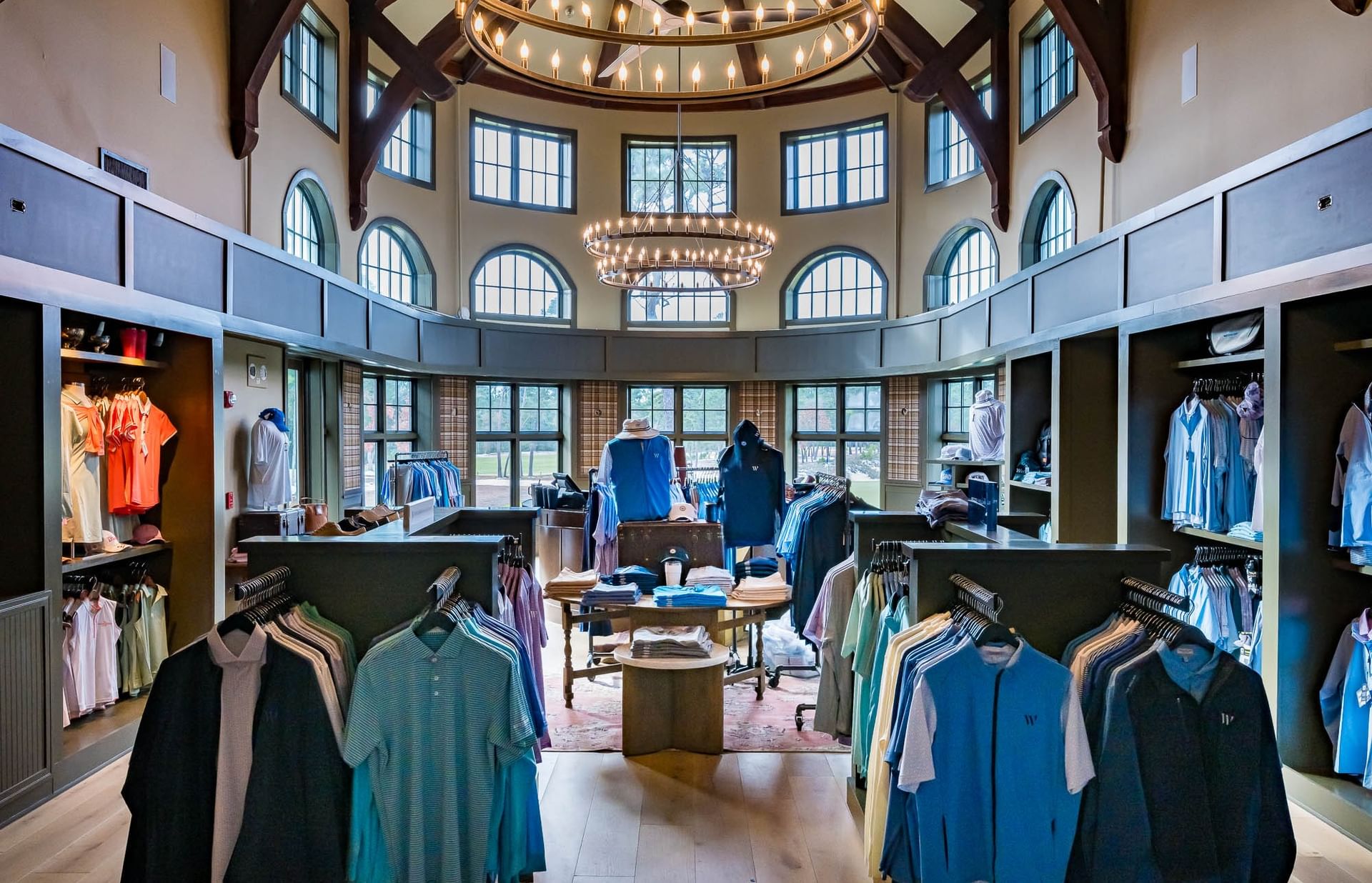 A clothing store with many clothes hanging on racks, a central table with folded clothes, and large windows.