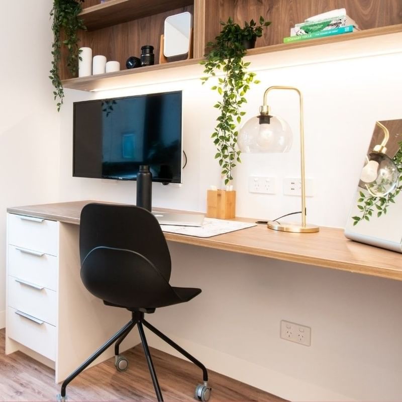A stylish office space with a desk, chair, monitor, lamp, potted plants, and a shelf with items and a framed picture.